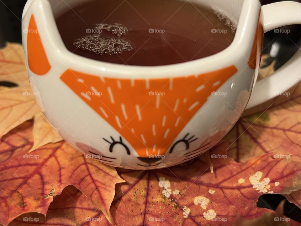 Fox-shaped mug with black tea on autumn coloured leaves.