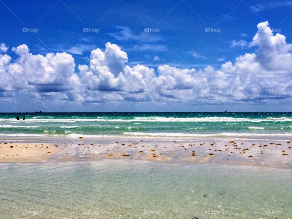 Sunny days: tranquil seascape landscape view to the horizon over the white sand beach and turquoise ocean under the bright blue sky with white cumulus clouds