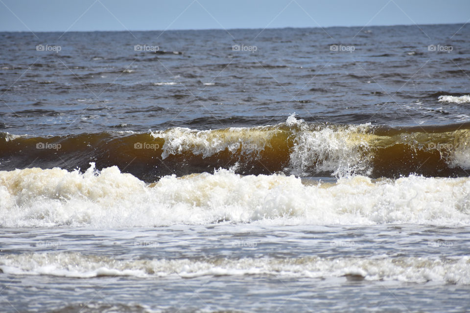 big wave in ocean near sandy beach with blue sky