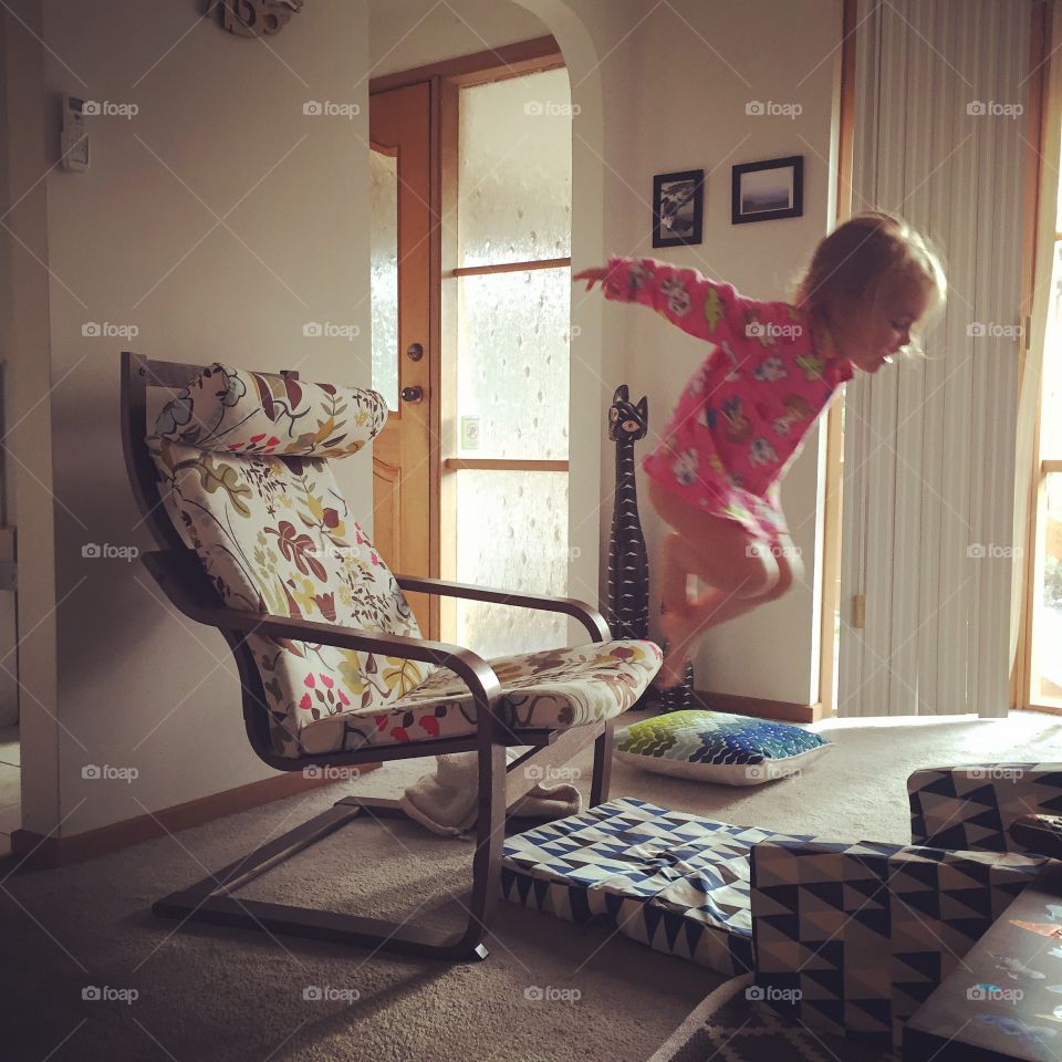 Small girl jumping over the cushion