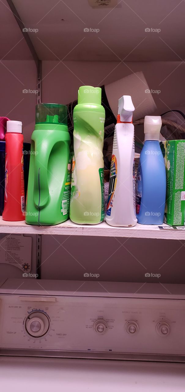 Different types of laundry detergent bottles and fabric softeners sitting on a shelf in laundry area.