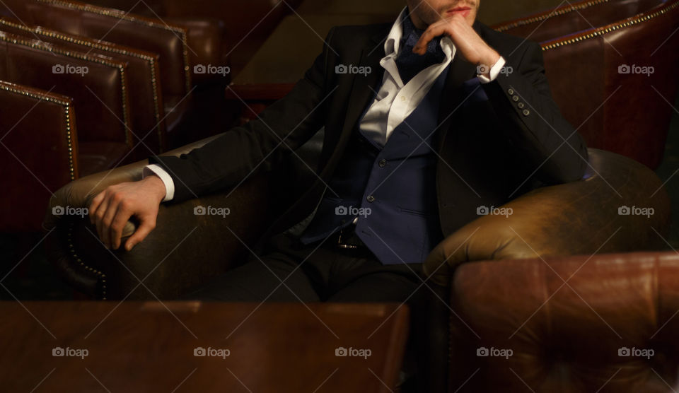 Men in costume, white shirt, sitting in the armchair