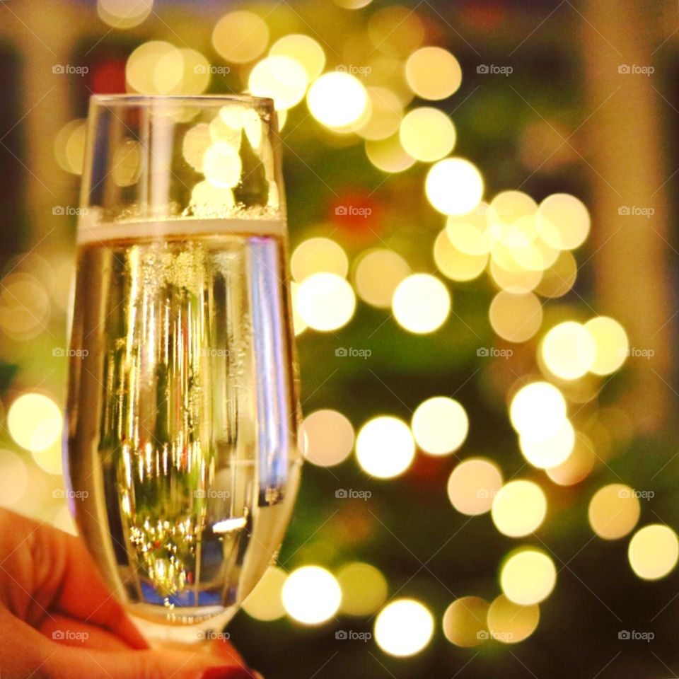 Glass of champagne in front of Christmas tree in cosy house. 