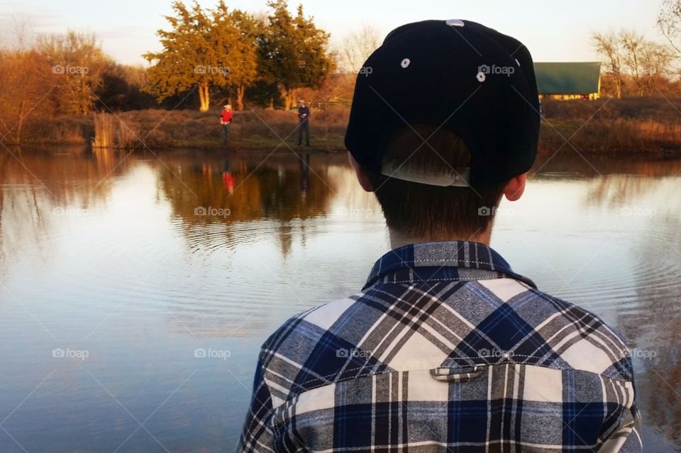 A young boy fishing looking across a pond at two other boys fishing in fall
