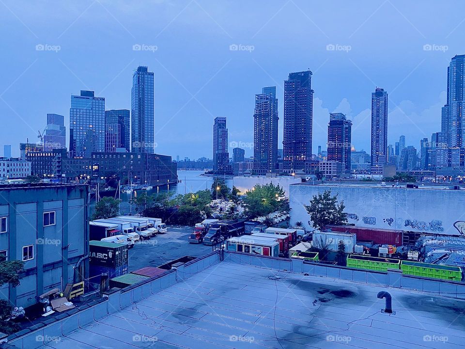 This is a view over LIC rooftops towards the “East River” at “Newtown Creek” by the “Pulaski Bridge”. On the left across the river you can see “Greenpoint”, Brooklyn and in the very fair distance there is “Manhattan”. 2023. Hypnotic Productions