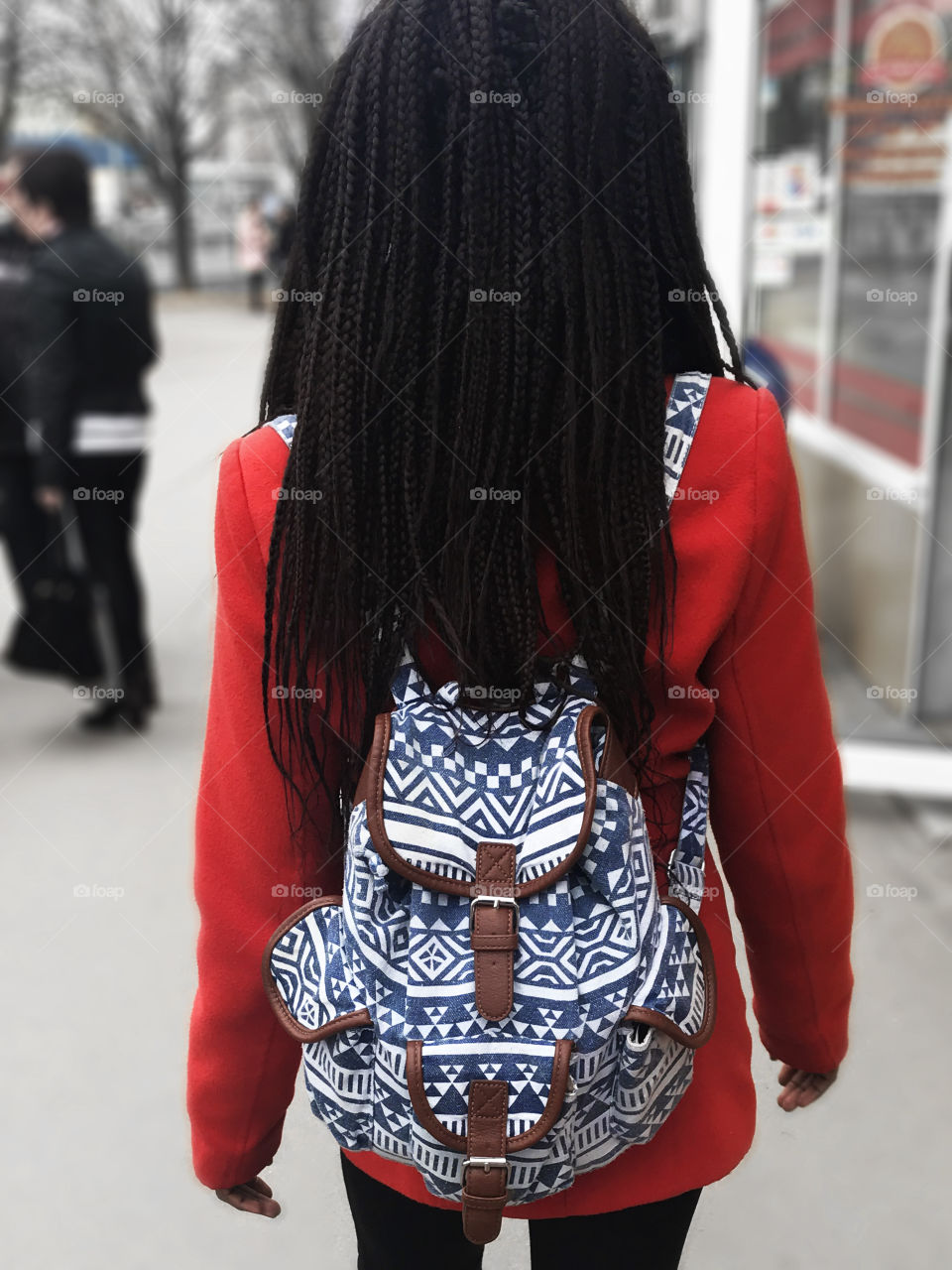 Young woman with stylish haircut in red coat with a blue backpack walking in the city 