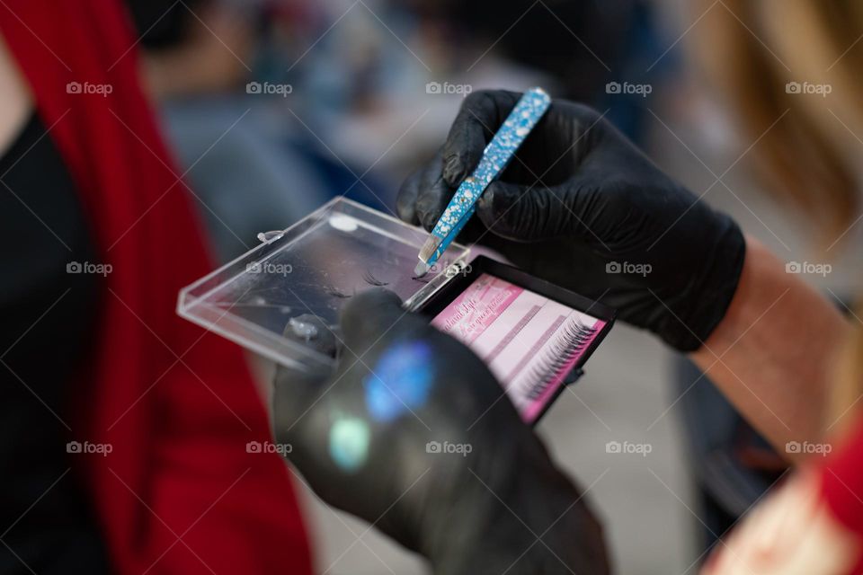 Hands in gloves applying artificial eyelashes