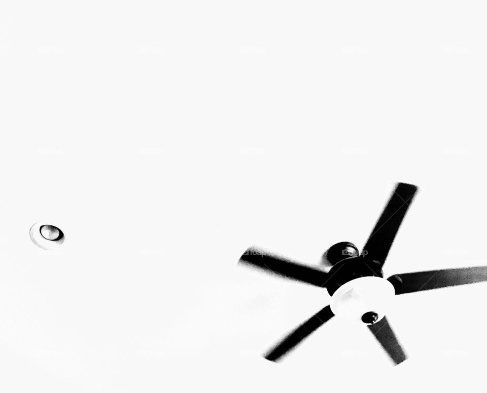 Abstract black and white photo of ceiling fan and can light on stark white ceiling. 
