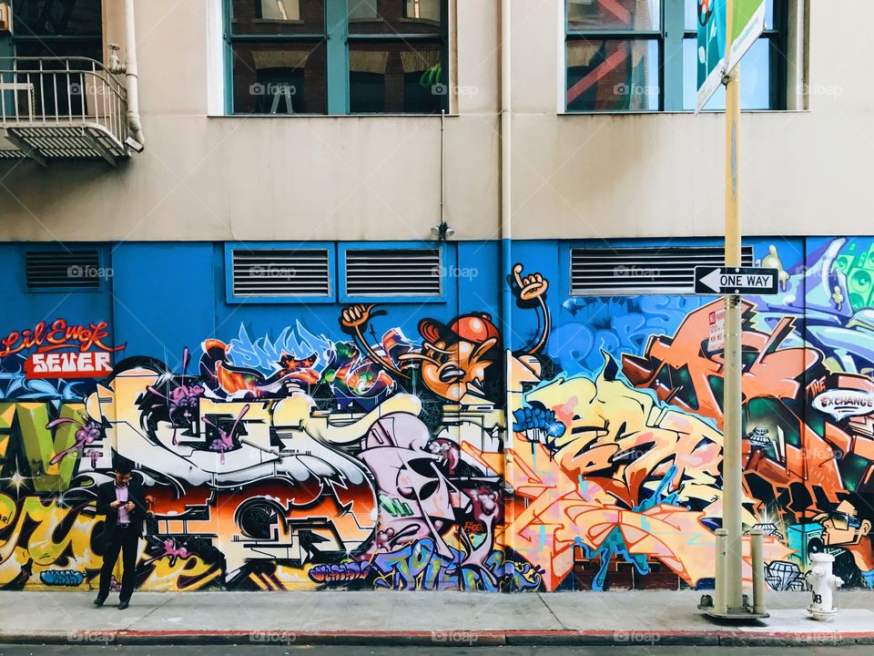 Man checking his phone in front of a graffiti mural on a wall in downtown San Francisco.