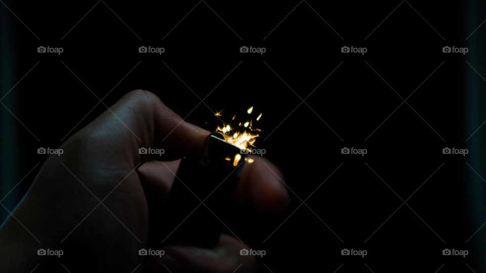 A person has lighters in his hands and he lights it through a flint wheel, the lighter ignites, sparks and fire appear, close-up on a black background.