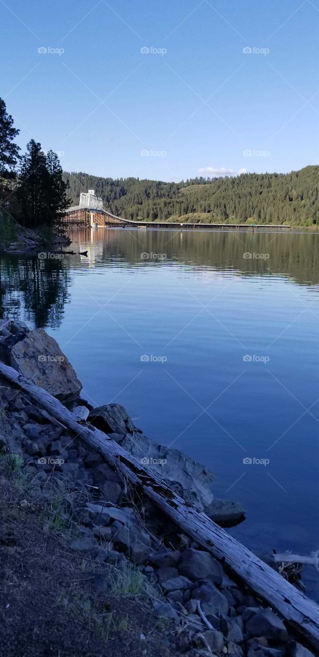shoreline view of a bridge over a lake with tree, mountain ridge and bridge reflection on the lake water