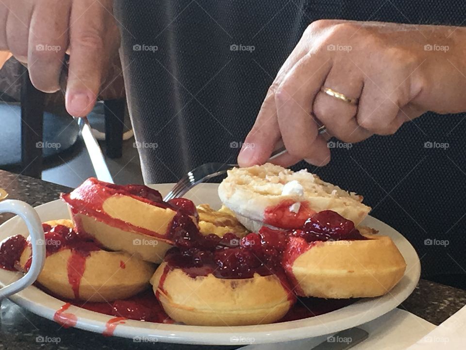 A huge and ample plate of round waffles for breakfast topped with fresh berries and whipped cream, closeup of man eating not showing face