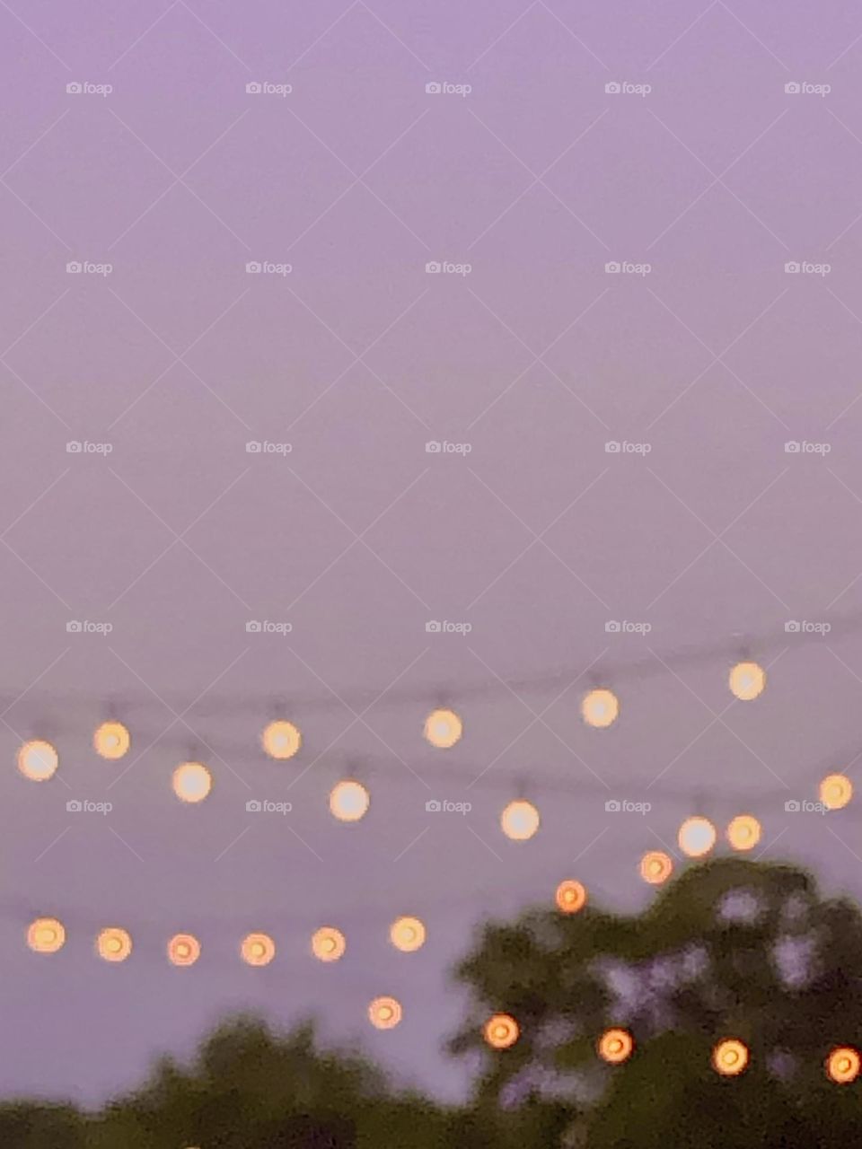 A polka dot of party lights against a hazy, lavender sky and above the green tree tops ☺️