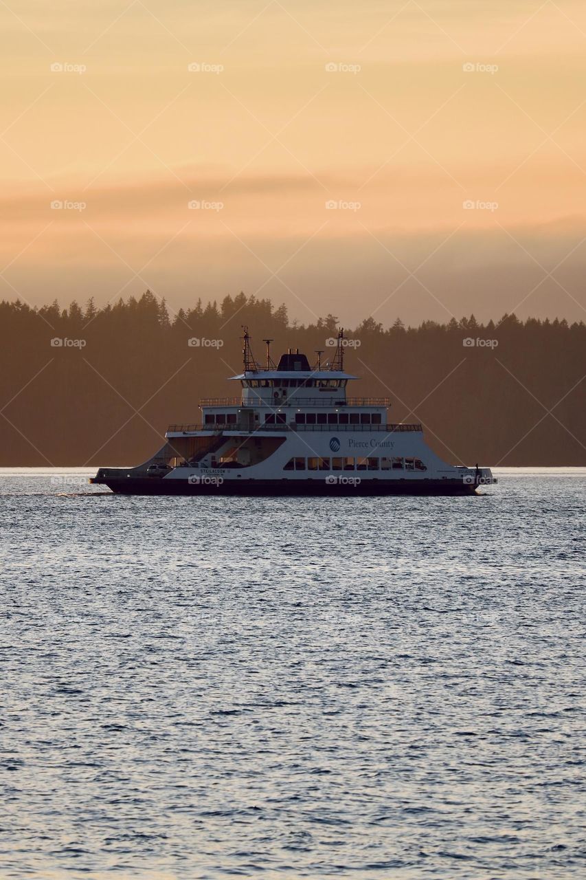 A commuter ferry travels across the calm waters of a Puget Sound inlet at sunset 