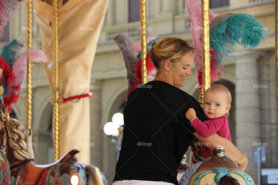 Happy mother trying to sit her child on ride