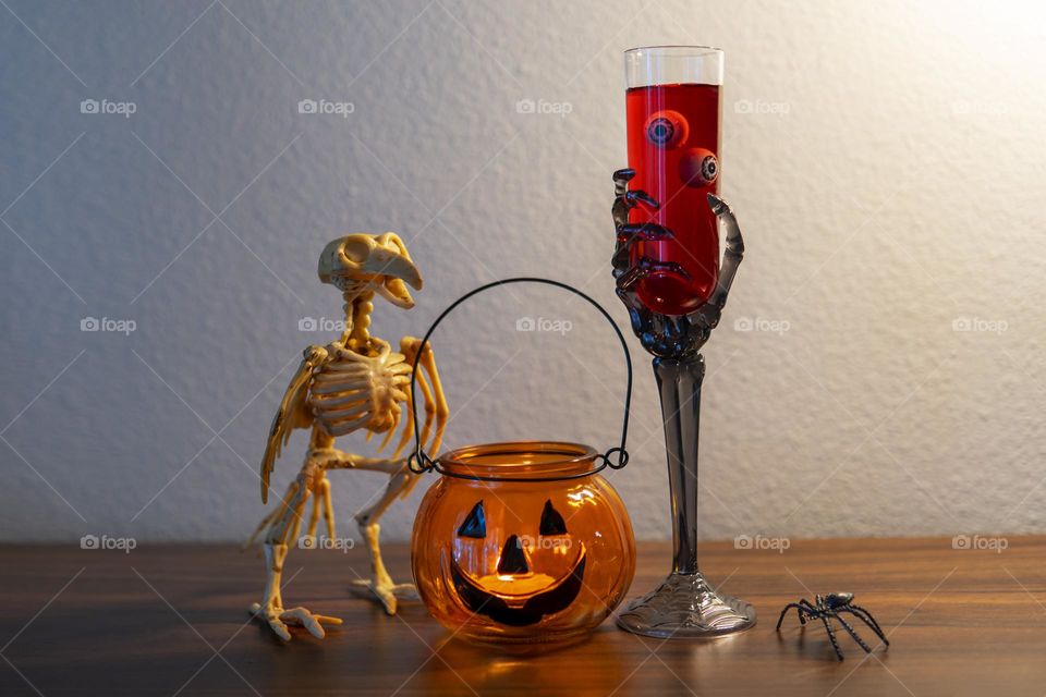 Halloween composition with bird skeleton, jack o lantern, spider and glass of wine with eyes balls 