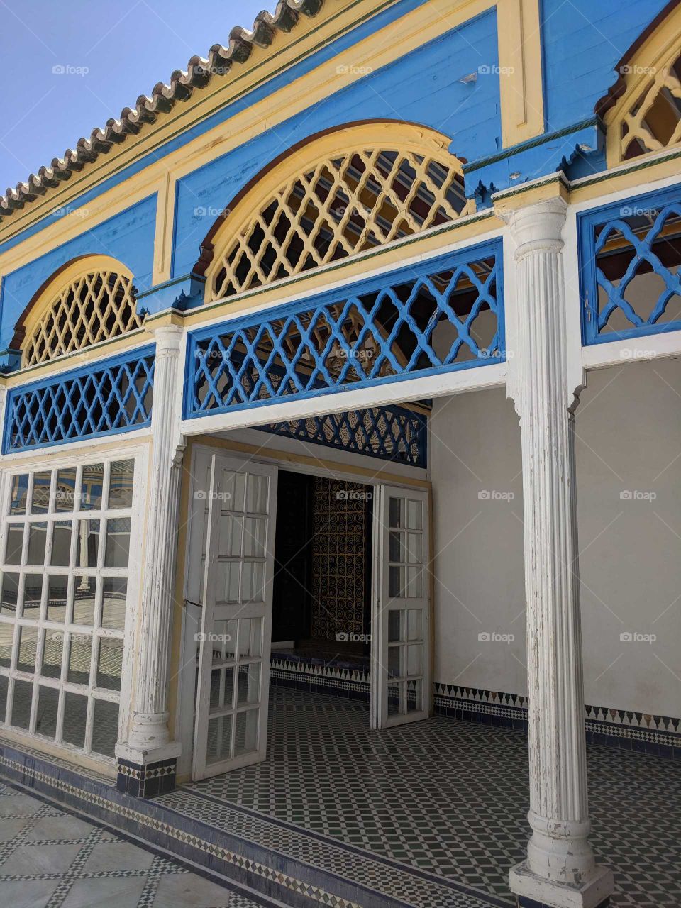 Beautiful, Ornate Blue and Yellow Detailing on the Arches Above the White Wooden Door (with Glass Windows) and Tiled Ceramic Mosaic Floors in the Courtyard of the Bahia Palace in Marrakech in Morocco