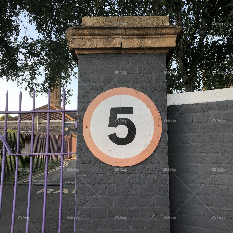 Number 5 circle road sign on a grey painted brick wall 