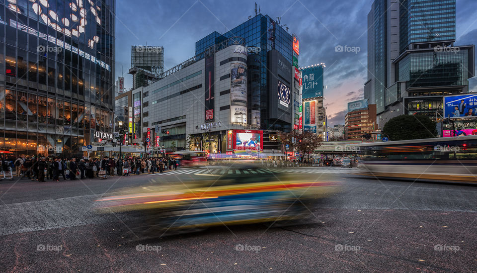 Japan traffic crossing the famous Shibuya crossing at blue hour with the setting sun in the distance 