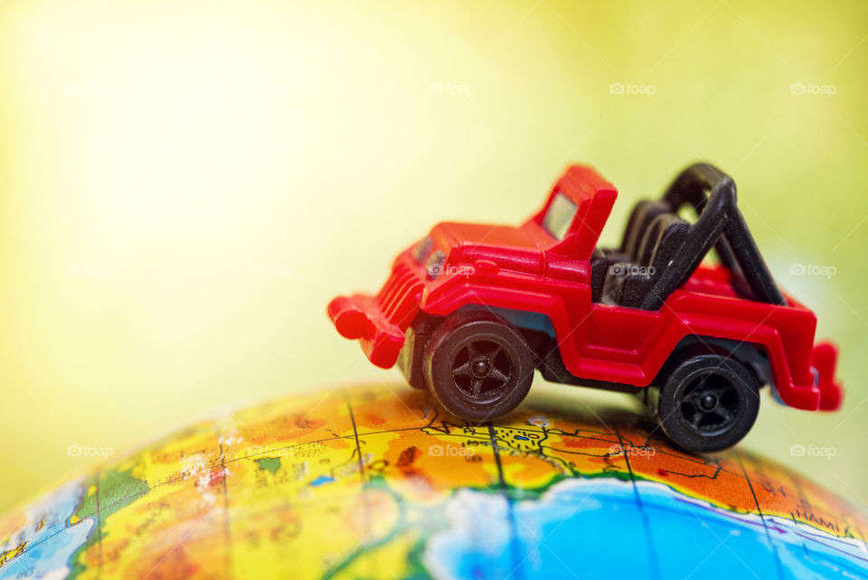 A red car on globe on green background with sunshine. Miniature car toy on globe. Travel concept