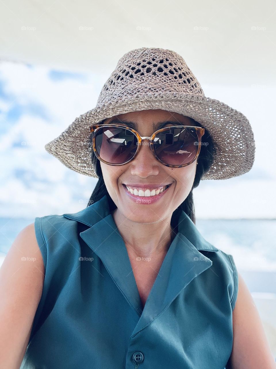 Selfie of a woman wearing brown sunglasses and gray hat riding on a boat against clouds background. 