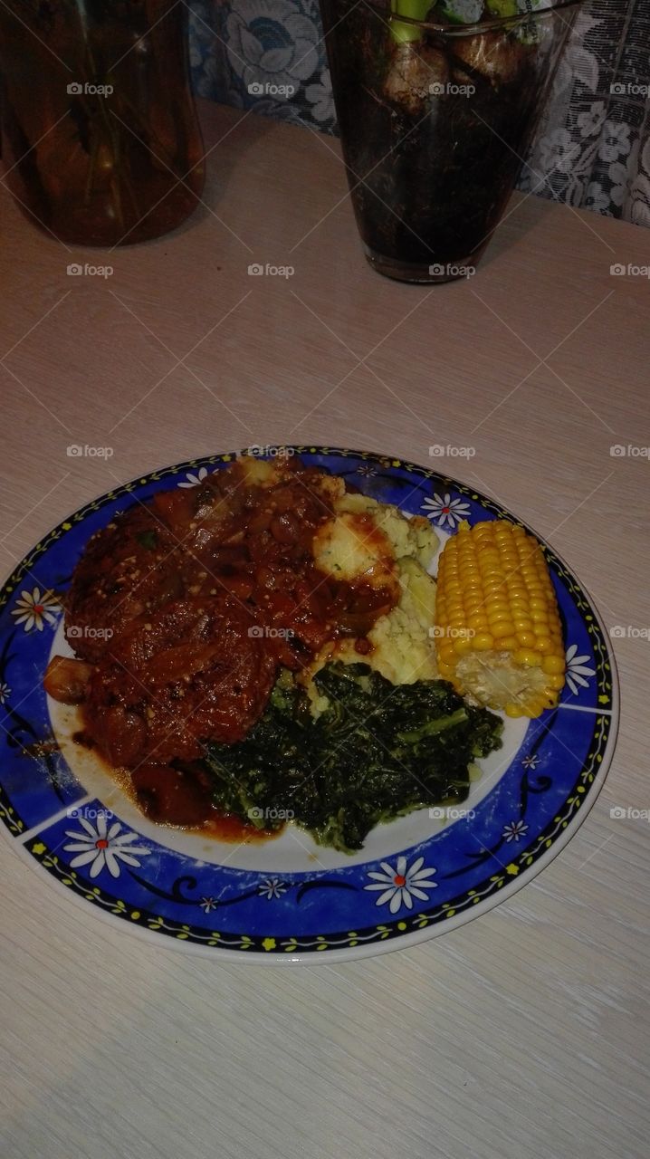 Nice plate. Dinner. You have corn on the cob. Sweet corn that is. Then you have mash potato with peterselie, spinache, and stew chicken.