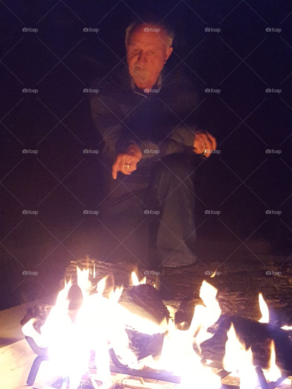 Senior man sitting near campfire at night