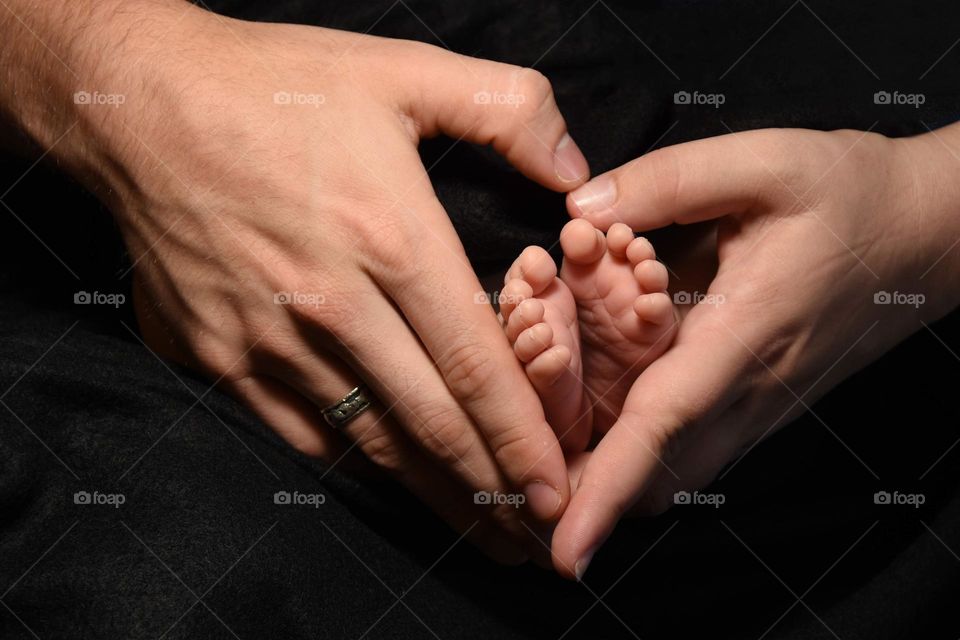 Mother and father making a heart with their hands with their baby’s feet in the center