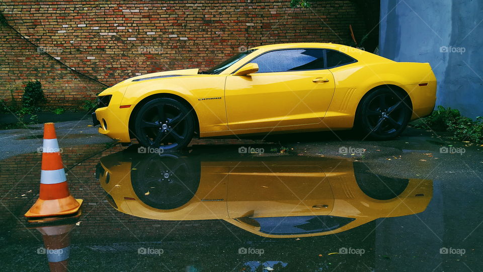 reflection of a yellow chevrolet car in a rain puddle