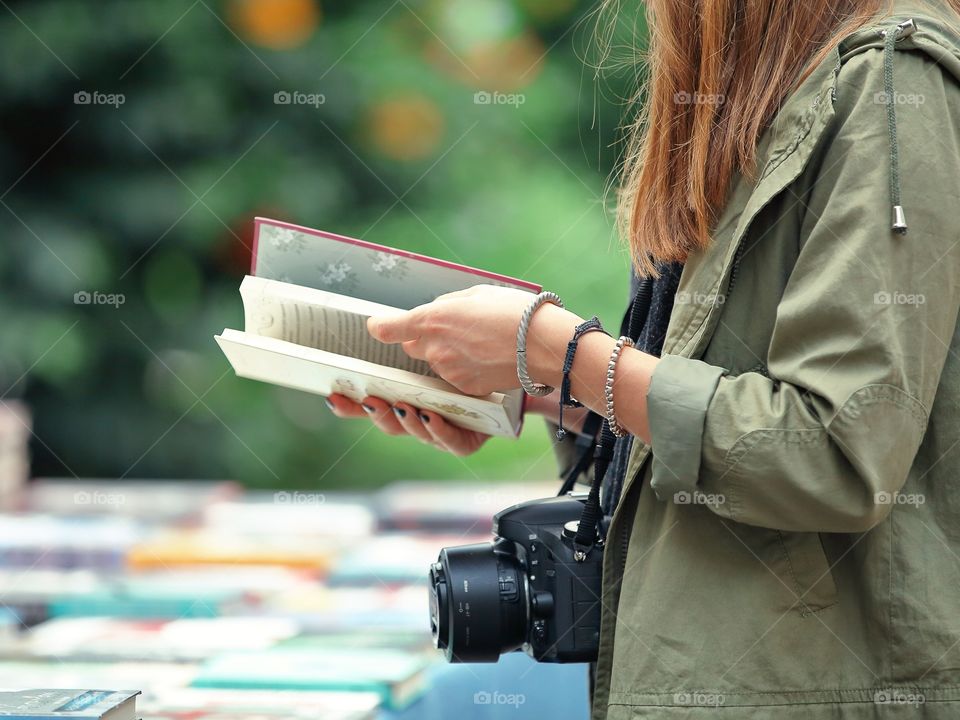 Girl-photographer reading a book on the book market 