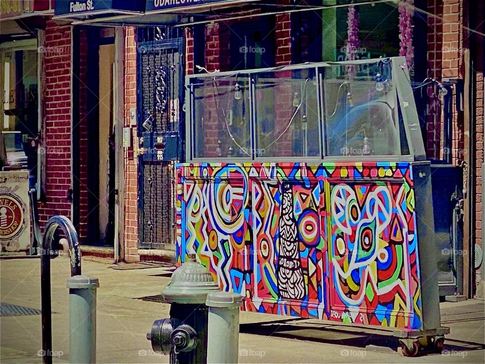 A colorful graffiti adorned board in front of an industrial NYC brownstone building somewhere in “Williamsburg”, Brooklyn. The multifaceted design reminds in style very much of the 1980s New York artist “Keith Haring”. 2022. Hypnotic Productions