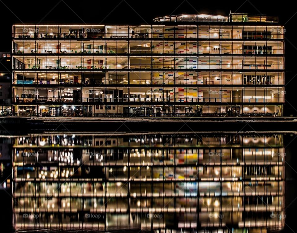 The combination of sharp architectural lines, colorful panels, and the serene reflection in the water contributes to a modern, sophisticated atmosphere.