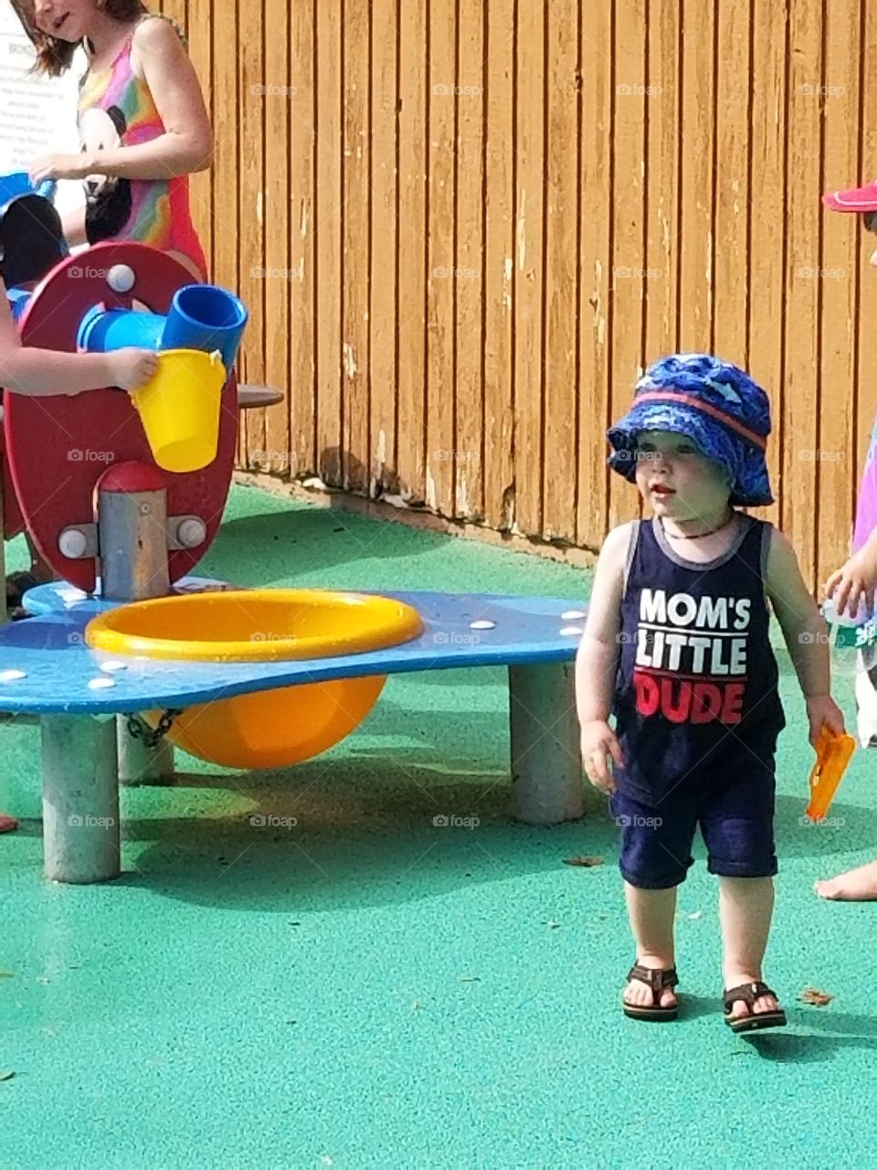 Cute little boy playing at the splash park with his water gun on a hot summer day.