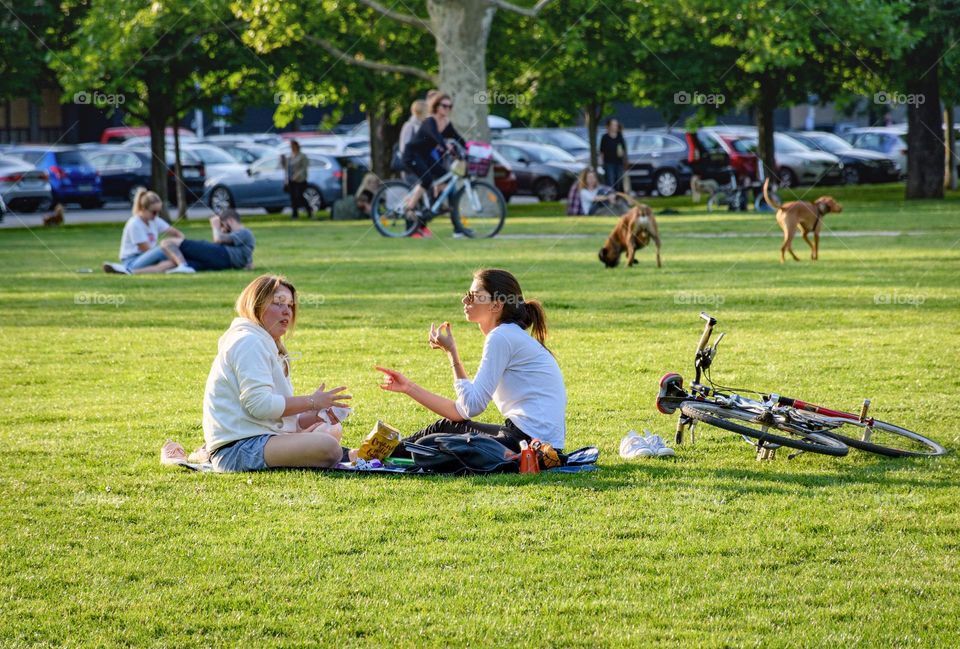 Two female friends sitting on blanket in park in city