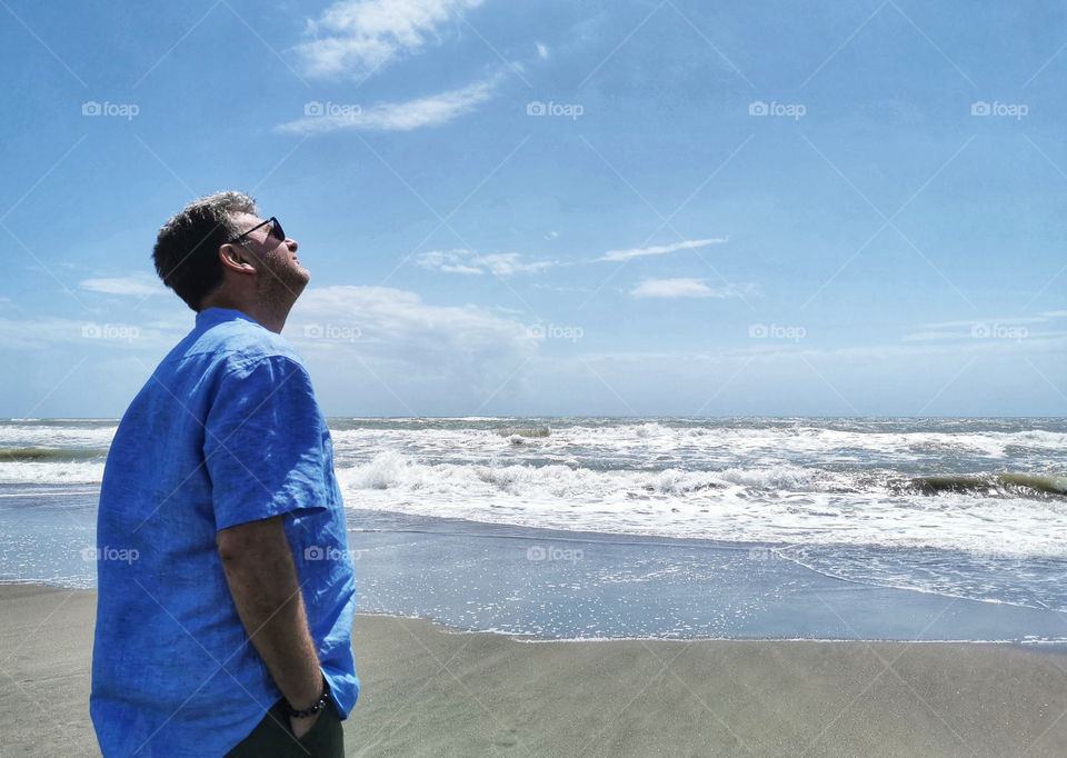 Man standing beside the beach looking up to the sky.