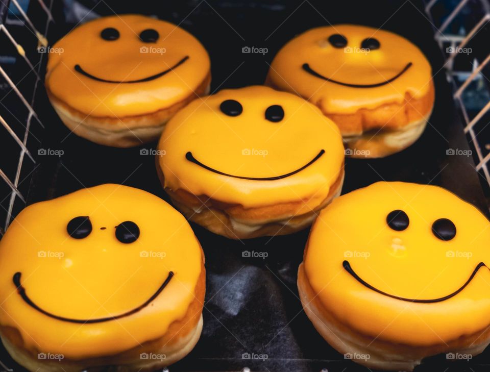 Cute donuts with yellow icing and a chocolate smile with eyes lie on the counter in a store in the city of Brussels, close-up side view.