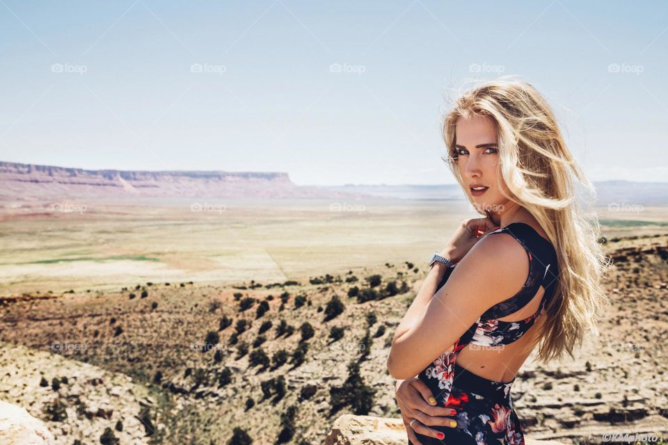 Young blonde female with long blonde hair  standing in a desert landscape with cliffs in the background.