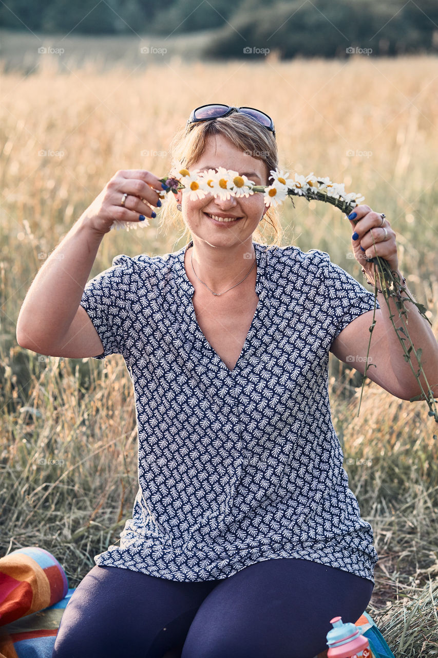 Smiling happy woman making coronet of wild flowers. Family spending time together on a meadow, close to nature. Candid people, real moments, authentic situations