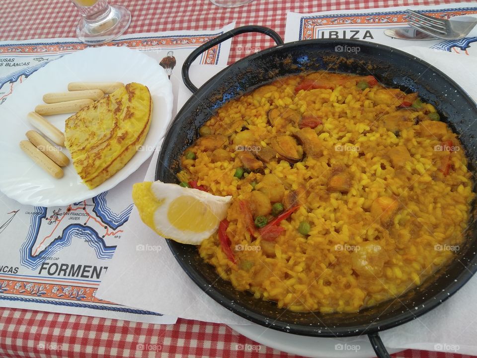 It is the nourishing and vibrant Paella dish in Ibiza. It is a Valencian dish. Paella is a Spanish rice dish that includes different combinations of vegetables and meats, characteristically seasoned with saffron.