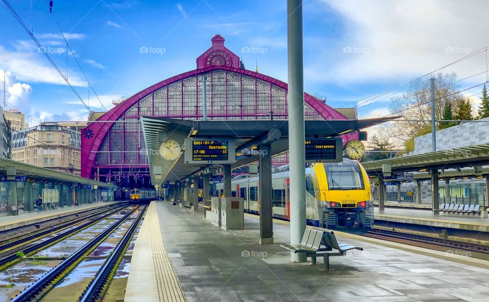 Antwerp central railway station under a blue sky after the rain with a train on the tracks next to the platform, waiting to leave