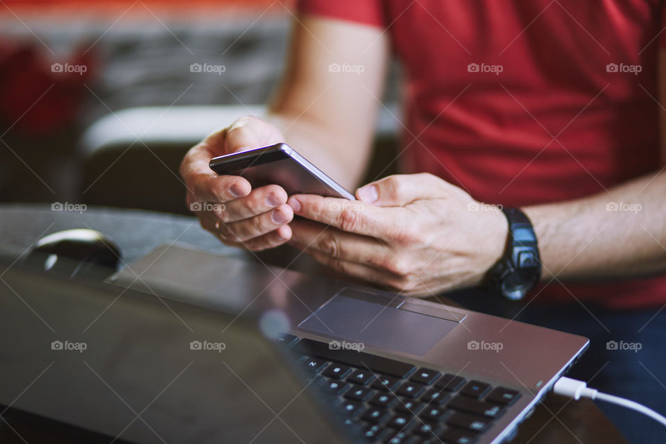 Man using smartphone working on laptop sitting at a desk