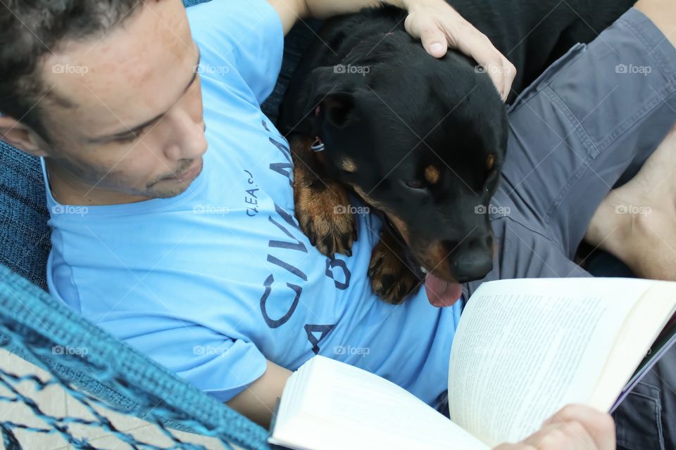He relaxes reading a book in the company of his Rottweiler