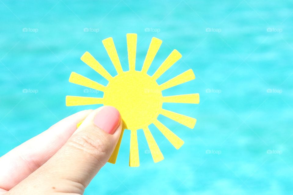 a woman's hand holds a yellow paper sun against the background of the pool