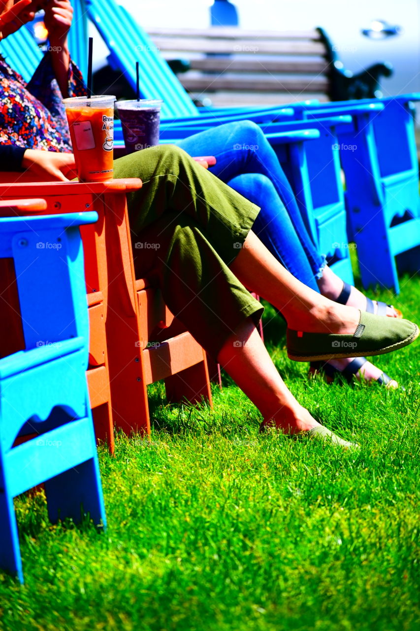 women sitting in lawn chairs on the grass. wearing sandals. drinking coffee.