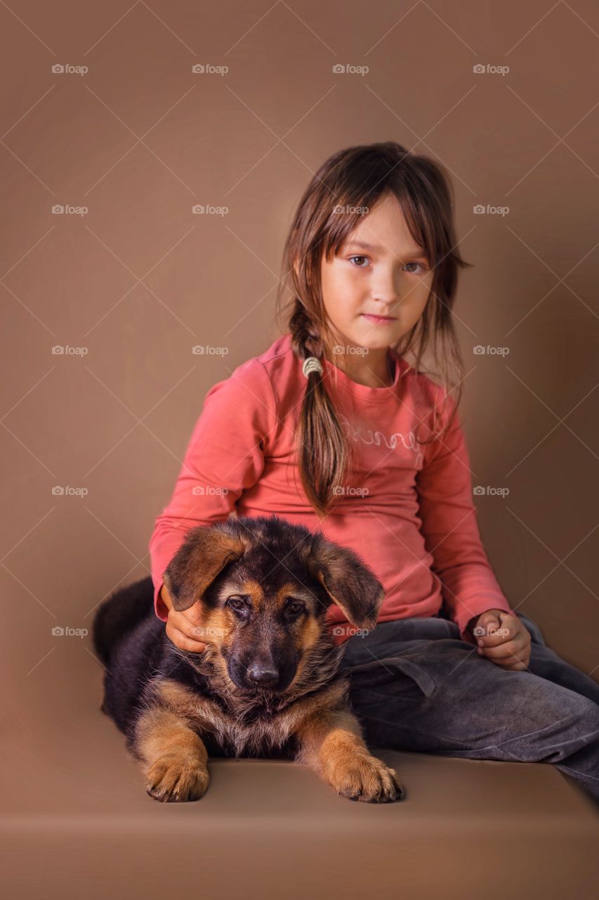 Little girl with German shepherd puppy on light brown background 