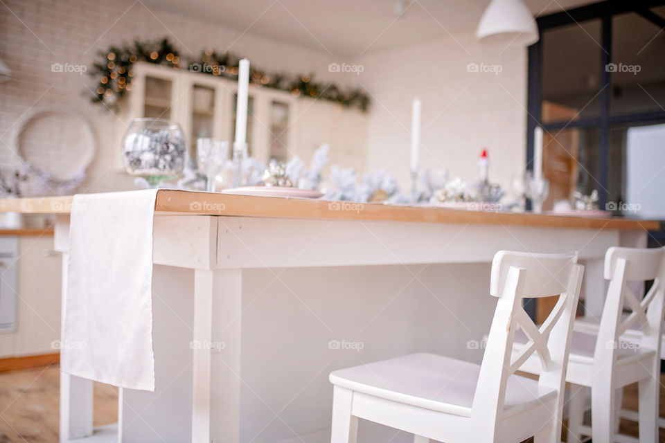 Festive winter cozy kitchen interior with garlands, decorations and gifts.  Christmas dinner at the decorated table.