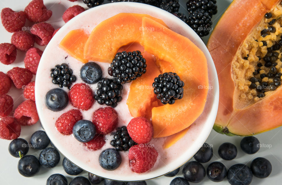 Yoghurt and fruit smoothie topped with berrirs and papaya