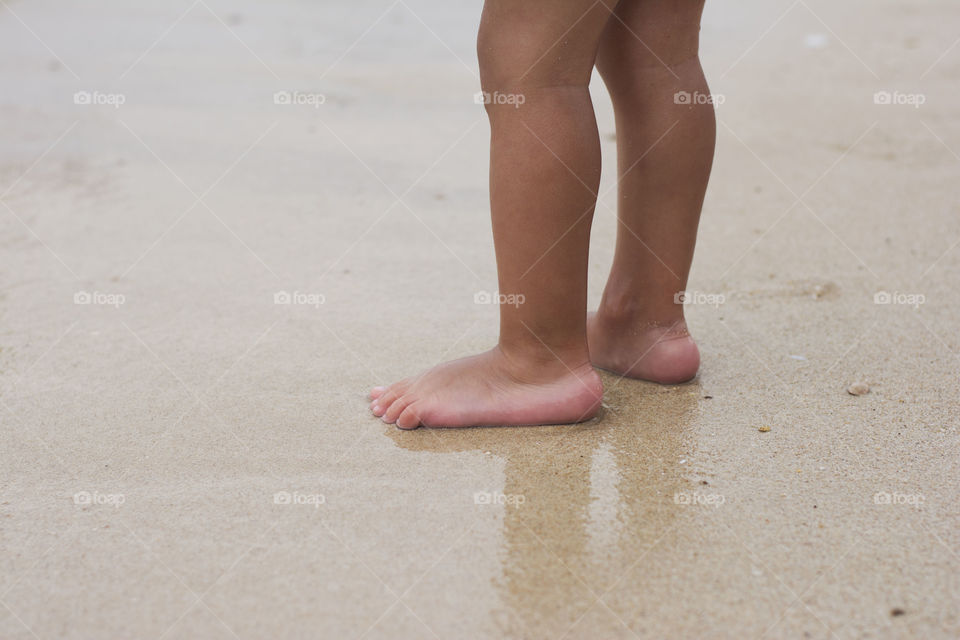 child feet in sand. child is standing barefoot in sand near water on beach