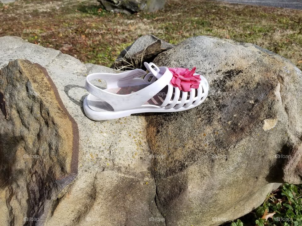 Looking for Cinderella. One, lonely, little, white shoe on a rock close to the police station. Some poor little girl can no longer enjoy her cute pair of shoes because thry are no longer together.