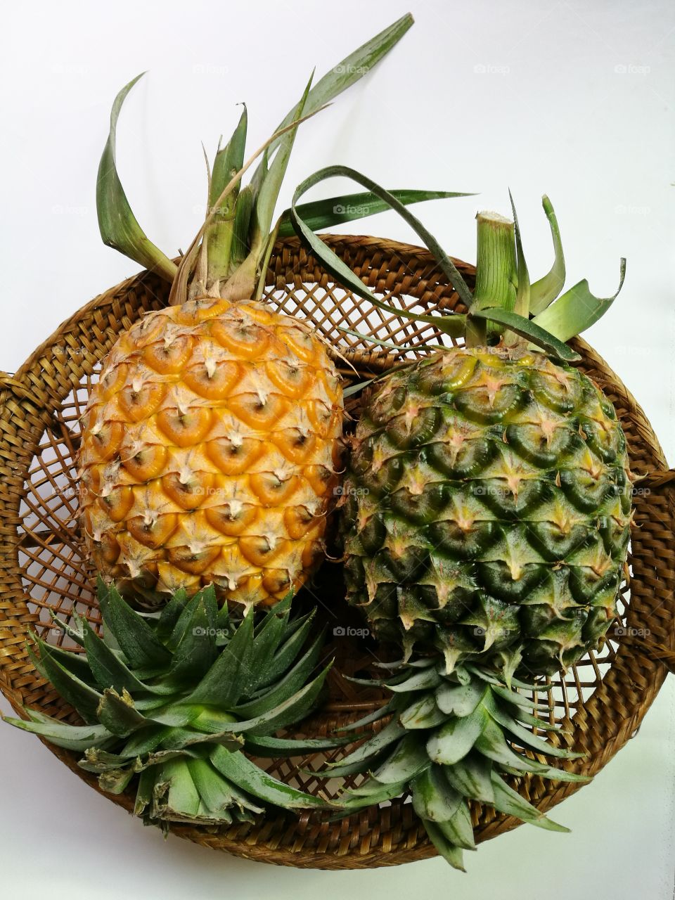 Top view of pineapples in rattan basket on white background.